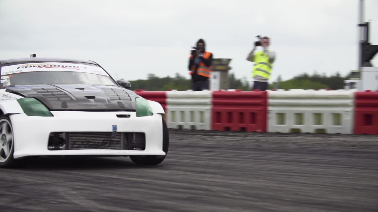 Nissan 370Z with trunk open and Nissan 280SX drifting on a drift track in super slow-motion with lots of smoke from the tyres and close racing.