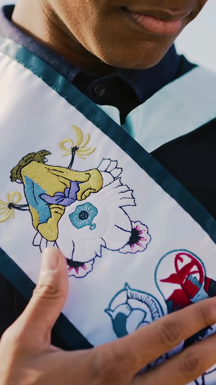 Vertical video: Looking down, graduate in gown sliding hand across sash outside, revealing patches
