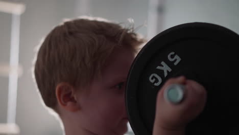concentrated little boy lifts heavy barbell with hands