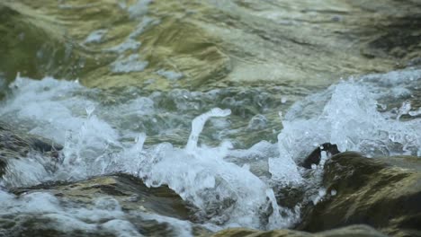 Primer-Plano-De-La-Ola-Rompiendo-En-Rocas-Oscuras,-Salpicando-Agua-En-El-Aire,-Gotas-De-Agua