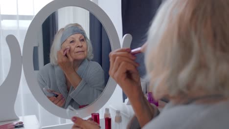 old senior woman grandmother putting makeup on, applying anti-wrinkle foundation powder with brush