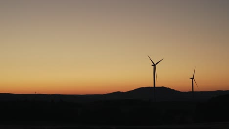 Statische-Aufnahme-Der-Silhouette-Zweier-Windkraftanlagen,-Die-Sich-Bei-Sonnenuntergang-Auf-Einem-Feld-Drehen