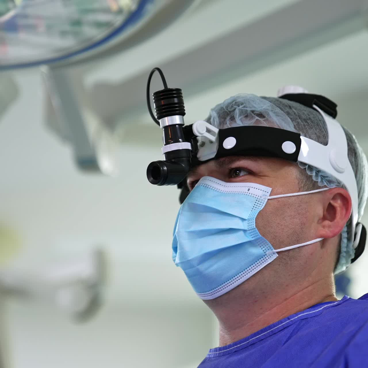 Concentrated look of a surgeon in mask, cap and headlight. Surgery professional close up portrait. Low angle view
