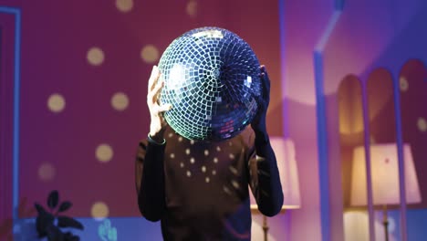 young stylish man holding disco ball in his hands standing statically in a retro party at home