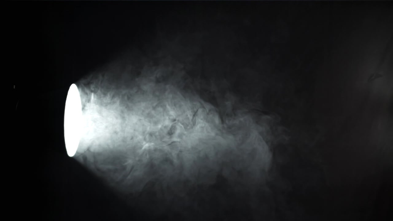 黒い背景に渦巻く煙を照らす明るいスポットライトの光