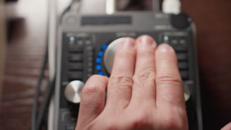 close-up of a hand operating a sound mixer, rotating a knob to the left to adjust audio levels. with the mixer s interface and various controls clearly visible