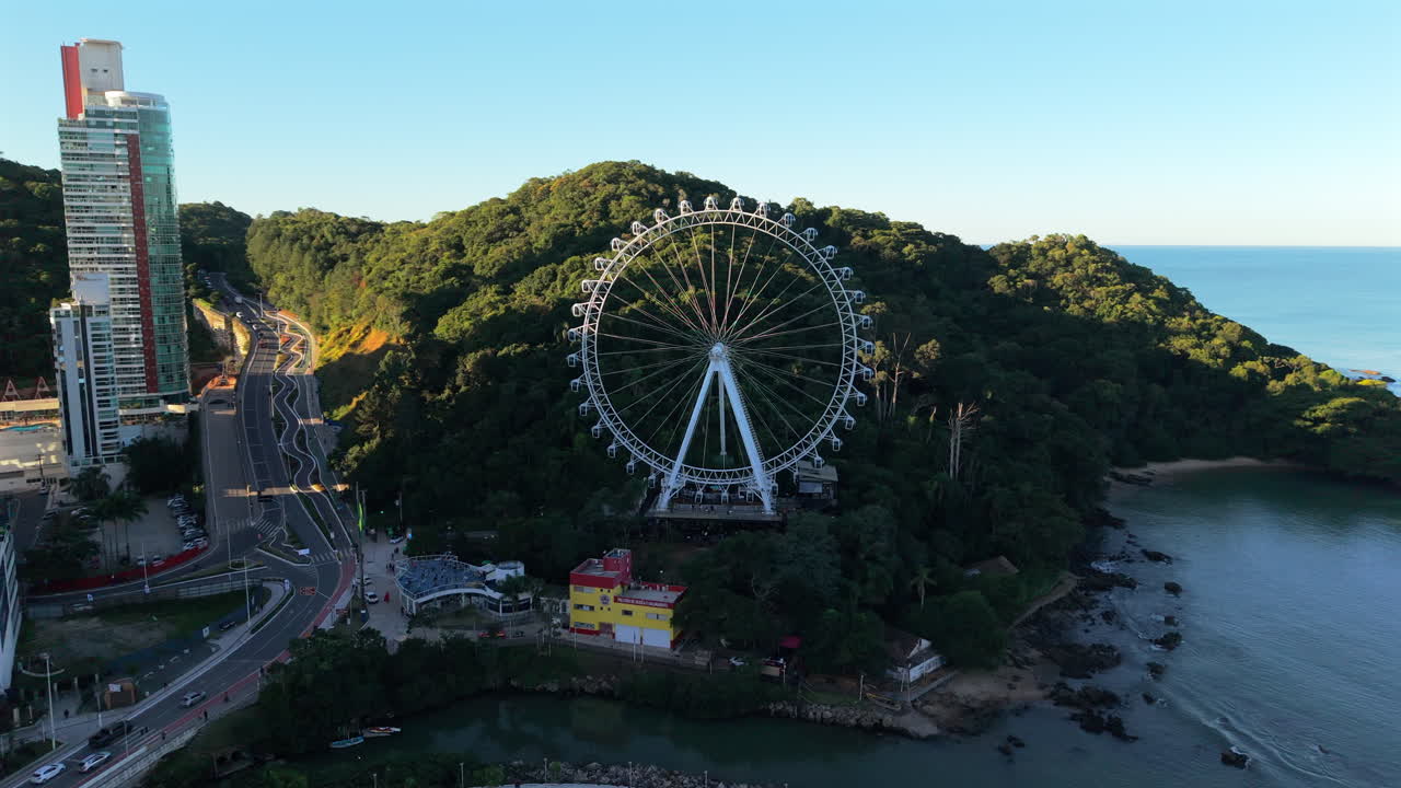 Forward drone shows Balneario Camboriu ferris wheel by beach and forested bay, late afternoon