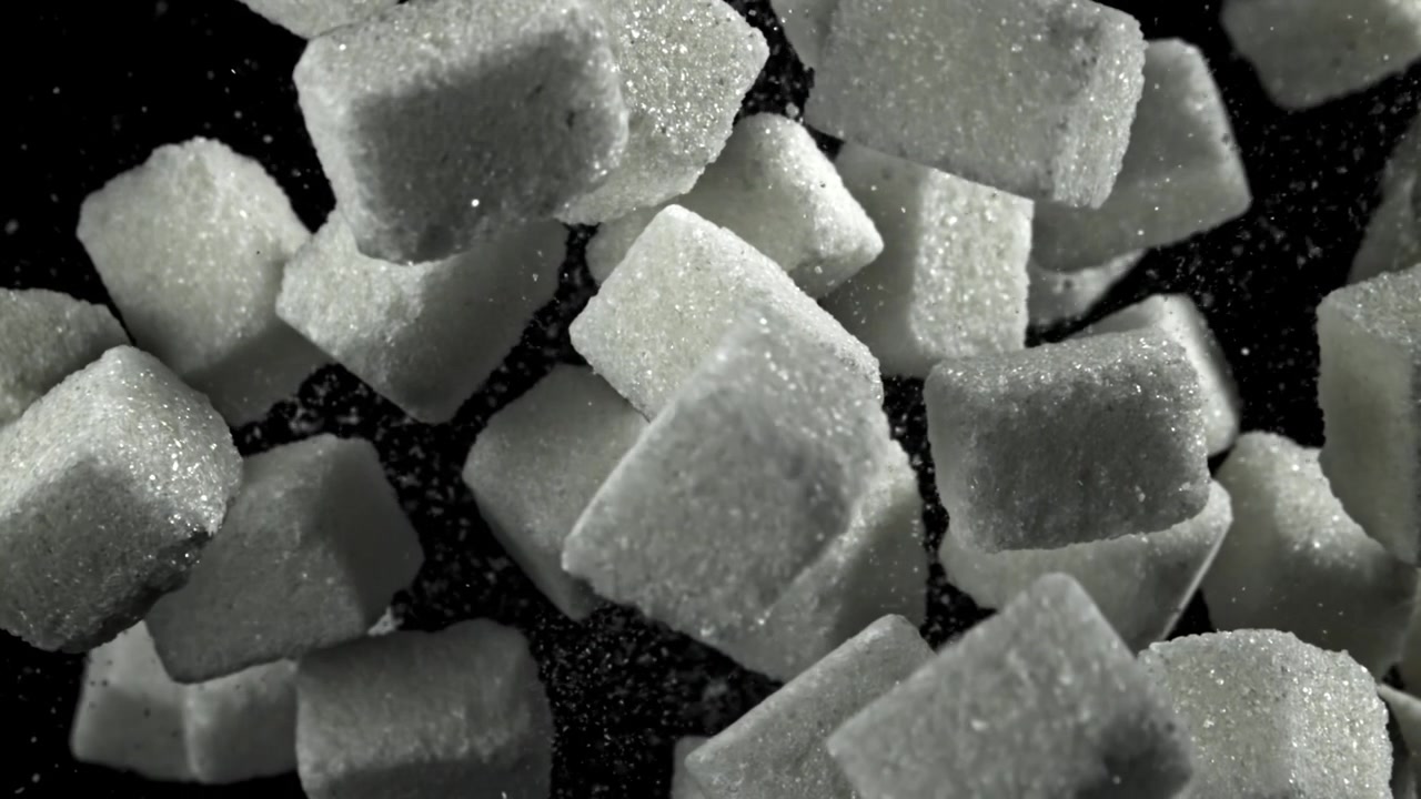 Sakte film av sukkerbiter som faller på svart bakgrunn