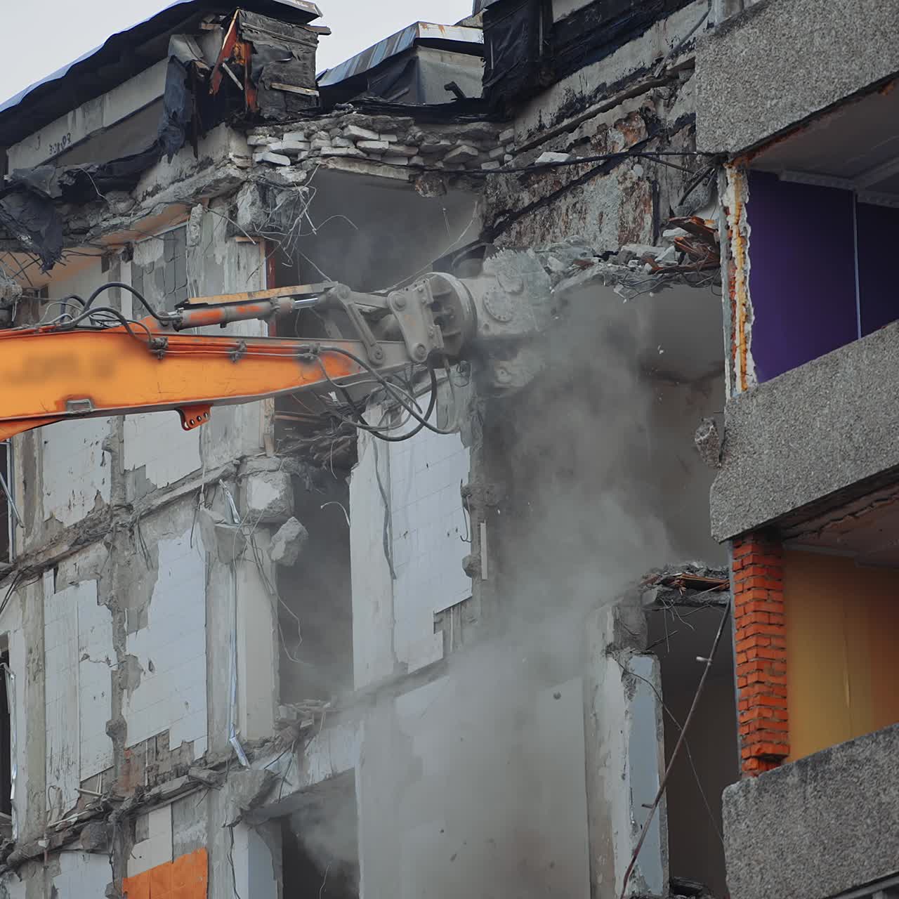 Hydraulic claw of excavator breaks easily the floors of an old building. Falling debris create thick dust cloud at the deconstruction site