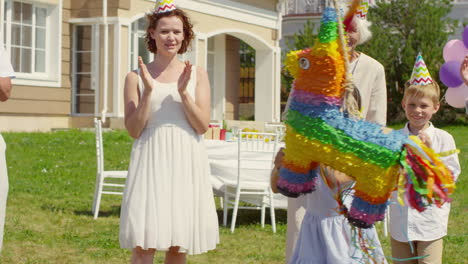 Happy-Multigenerational-Family-In-Party-Hats-Clapping-Hands-And-Smiling-While-Watching-Little-Girl-Striking-PiâˆšÂ±Ata-With-Bat-At-Birthday-Celebration-Outdoors-On-Summer-Day