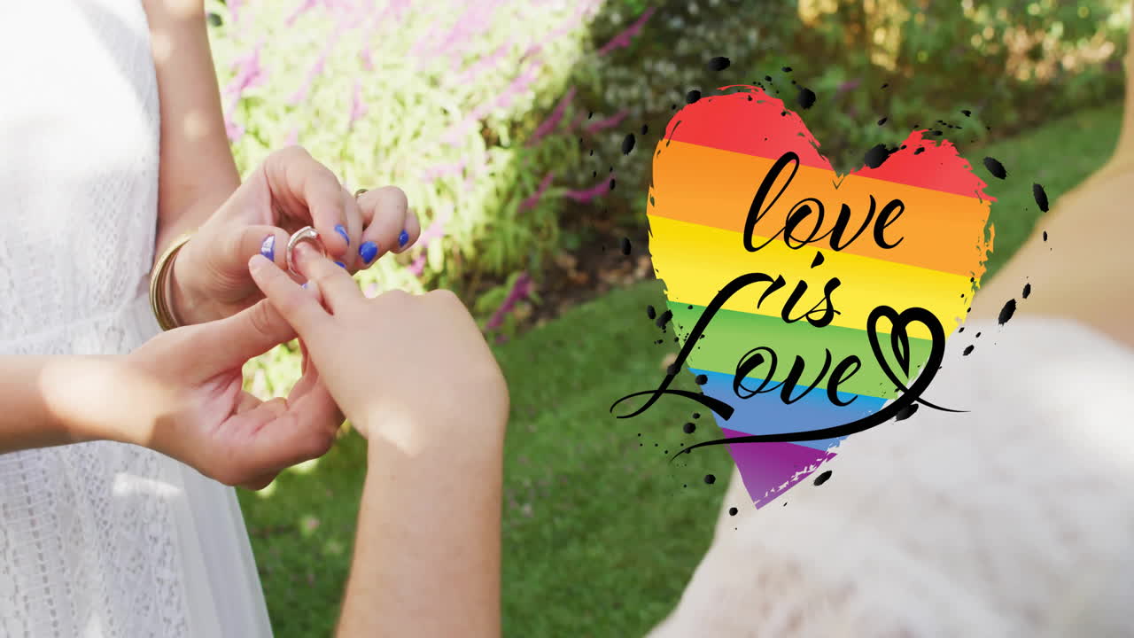 Animation of rainbow heart with love is love text over diverse female couple proposing