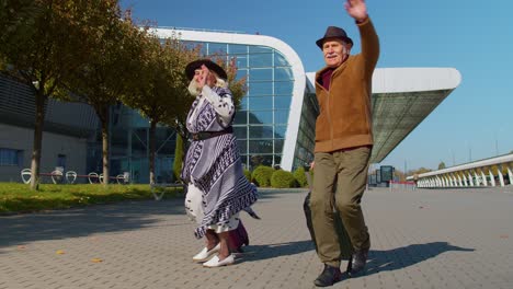 family grandmother grandfather walking with luggage suitcase bags to airport hall, celebrate dancing