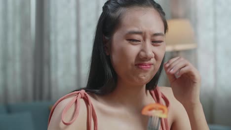 close up de una mujer asiática sosteniendo su mejilla y sacudiendo la cabeza debido a odiar comer comida saludable mientras come en casa