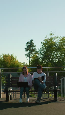 los estudiantes de secundaria estudian al aire libre; una niña con una computadora portátil en las piernas, un niño tomando notas, en medio de la vegetación y los postes de luz que mejoran el entorno académico pacífico