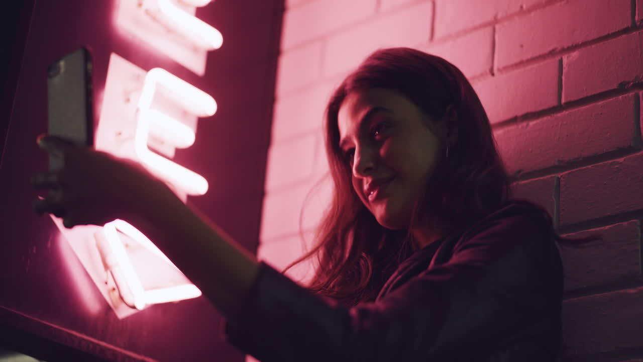 밤 에 네온 표지판 앞 에서 셀피 를 찍는 여자