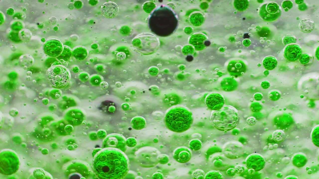 하나의 큰 검은 거품이 천천히 땅으로 떨어지는 물에 있는 녹색 거품의 매크로 샷