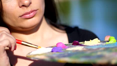 summer,outdoors, close-up of a palette with paints, the woman artist mixes paints with a brush on the palette