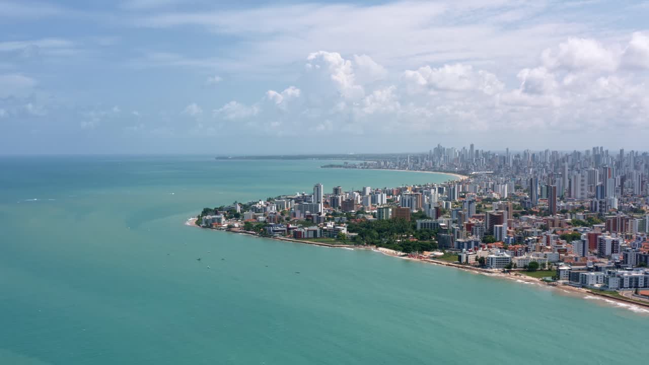 Dolly in aerial wide shot of the tropical capital of Joao Pessoa from intermares beach in Cabedelo, Brazil with skyscrapers along the coastline in the state of Paraiba on a warm sunny summer day