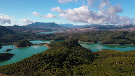 Aerial-drone-shot-of-a-cyan-coloured-lake-surrounded-by-forests-and-mountains