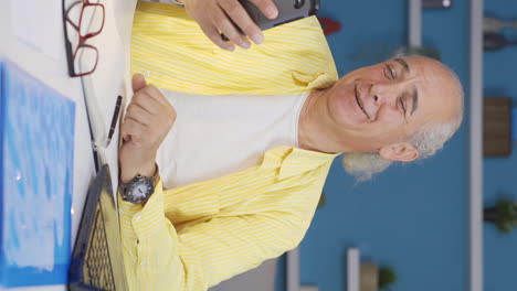 Vertical-video-of-Old-man-working-from-home-enjoys-mobile-apps-on-phone.