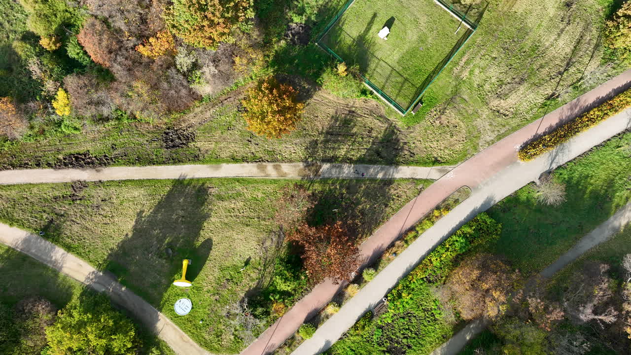 Drone top-down view of winding paths, grassy slopes and outdoor sculptures arranged within a natural park landscape