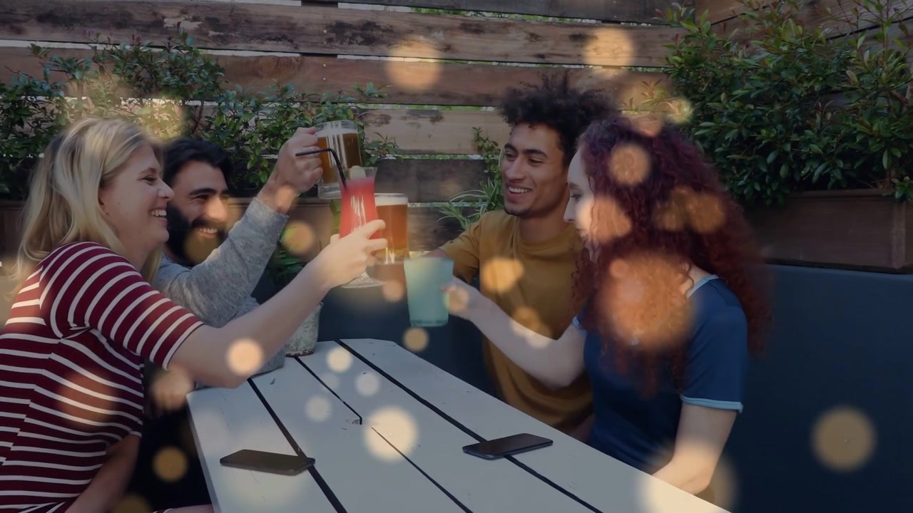 Venner hæver kopper, skåler og jubler, rækker ud efter snacks med bokeh-effekt over terrassen, til markedsføring af telefoner.