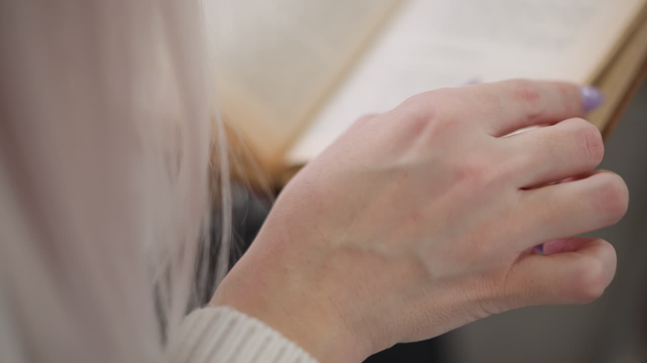 close up of woman hands with manicured nails gently flipping pages of hardcover book on bench in shopping mall creating serene and immersive reading moment in blurred modern retail environment