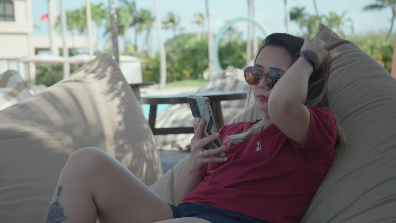 foto estática de una niña sentada y relajada en una bolsa de frijoles mientras usa su teléfono celular durante unas vacaciones