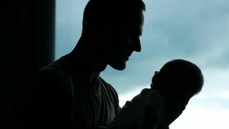 silhouette of a man holding a little baby. loving father kissing his adorable child. window at backdrop.