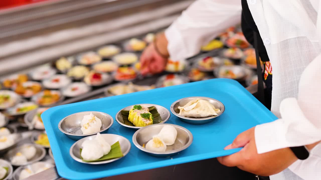 A vendor arranges steamed dim sum dumplings on a tray in a bustling Phuket market. Bright lighting highlights the vibrant scene