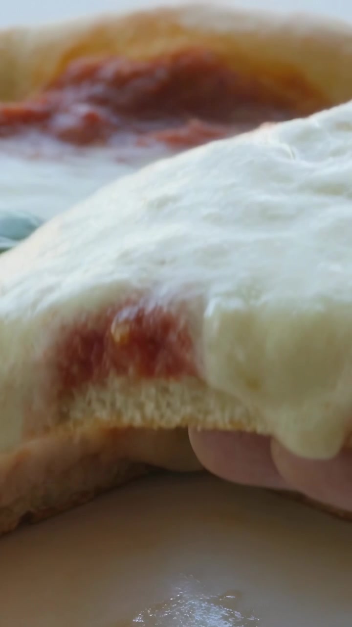 Video verticale: Una mano entra e solleva una fetta di pizza Margherita dal tavolo per mangiarla, con mozzarella che si allunga e basilico.