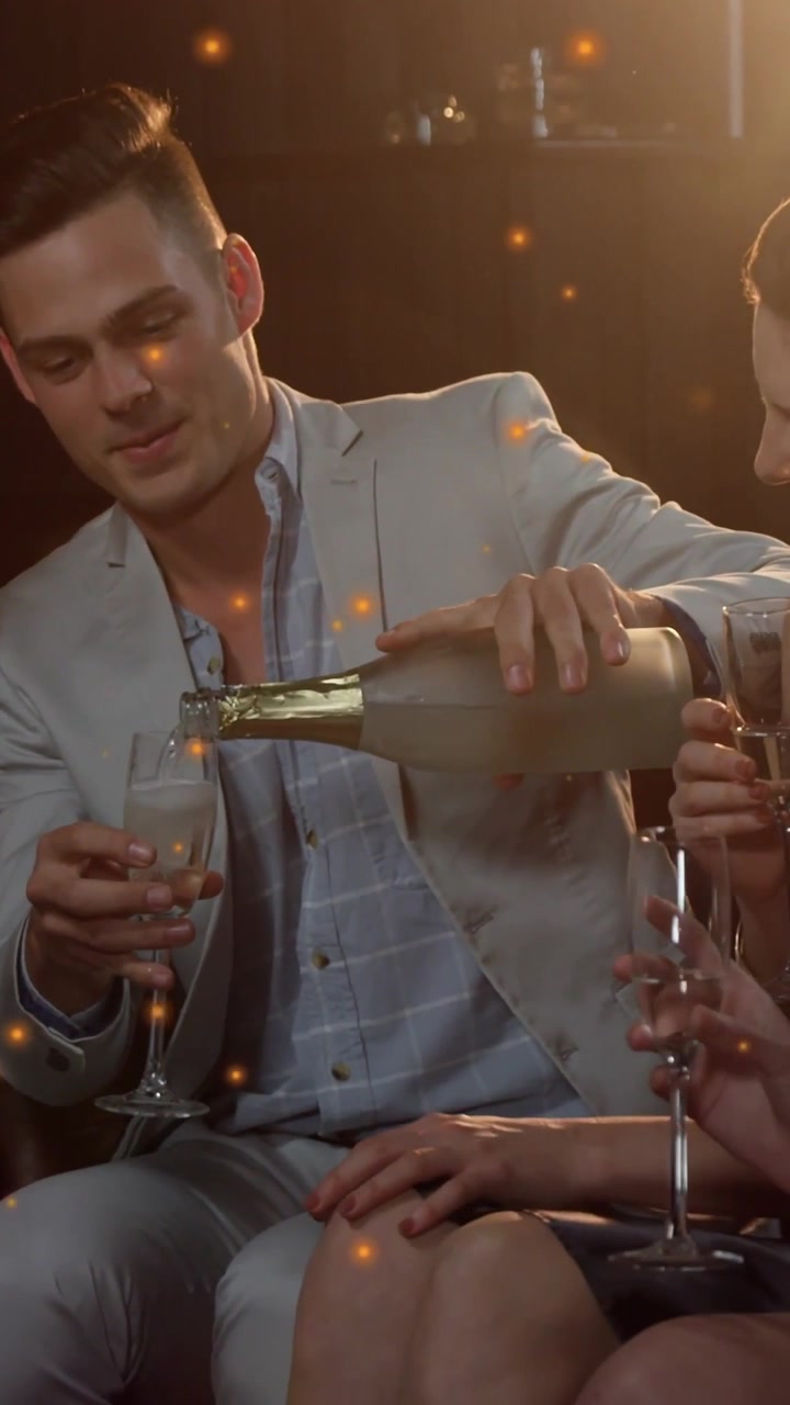 Vertical video: Man pouring bubbly in party bottle guests lifting flutes toasting bokeh floating
