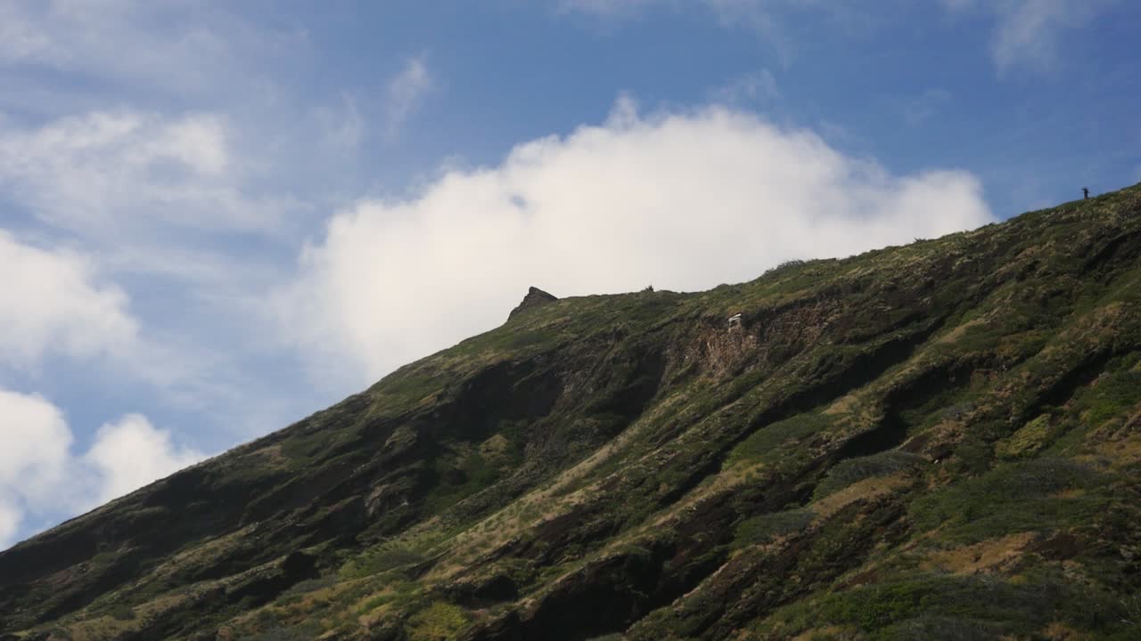 un excursionista solitario se para y examina la vista desde lo alto de un afloramiento de oahu con cielos azules y nubes detrás