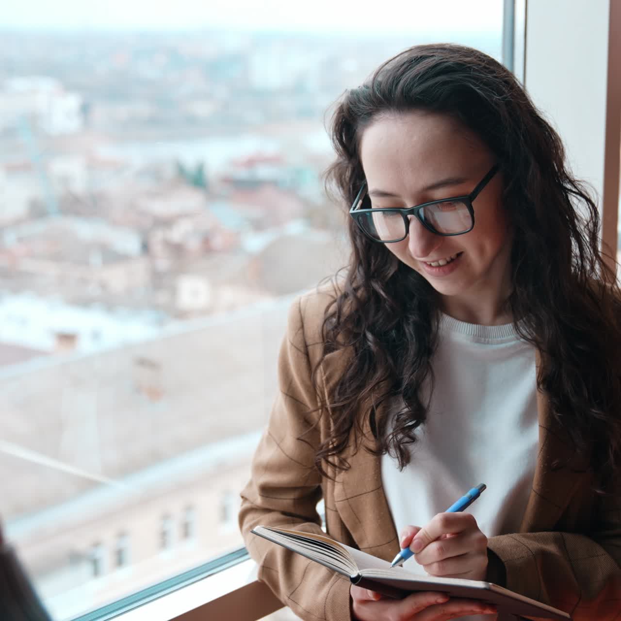 Secretary taking notes into paper notebook. Pretty brunette stands at the window, listens to her manager and writes down. View from top