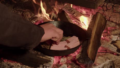 thick ham slices added to buttered cast iron pan on hot camp fire logs