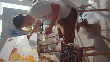 young male artist sitting on chair and painting in art studio