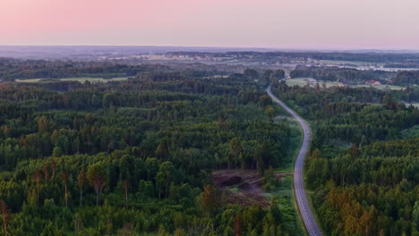 drone shot of countryside road winding through green forests in early summer morning fog