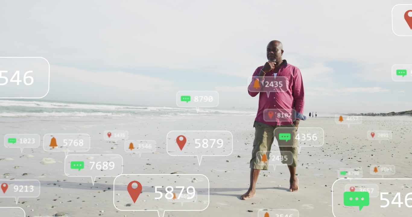 Senior man walking along sandy beach while taking call, mobile tech alerts clustering around feet