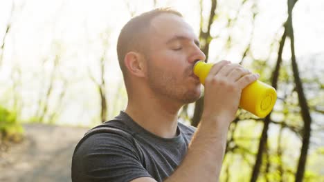 enjoying a break during a hike, a man drinks from a yellow bottle outdoors