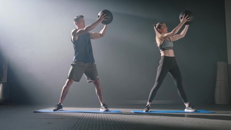 Reacting to cue, trainers in-gymwear doing medball lunges on blue mats in-gym-studio for training