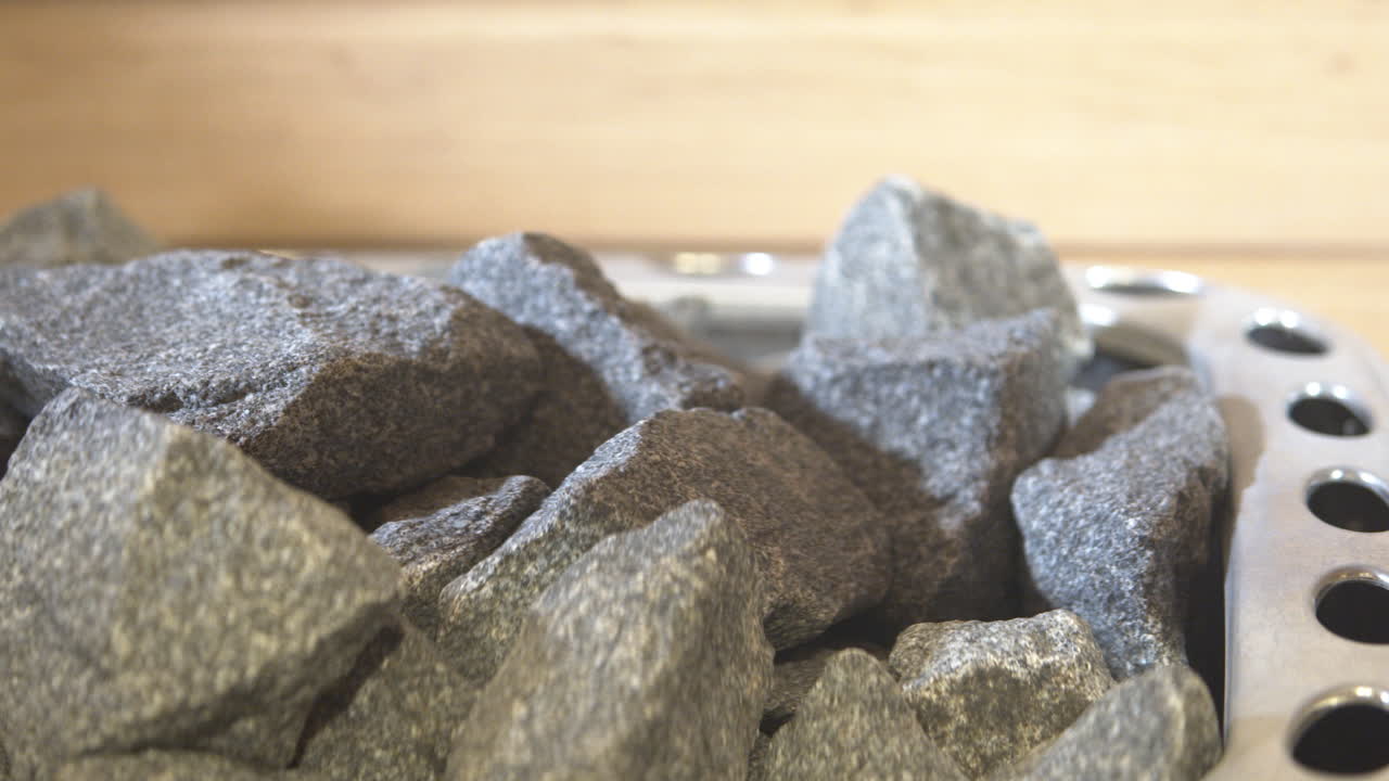 나무 사우나 안에 있는 뜨거운 돌을 보여주는 근접 촬영 트럭, 검은 돌을 가로지르는 트럭