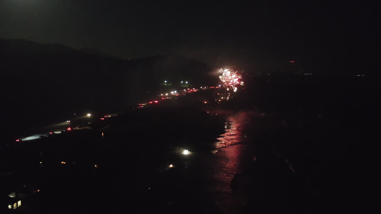 Night Fireworks Display Over Beach and Ocean with Road Lights