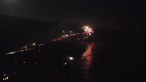night fireworks display over beach and ocean with road lights