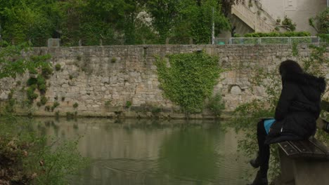 Mujer-Con-Estilo-En-Un-Banco-Mirando-Tranquilamente-El-Paso-Del-Pato-En-El-Río-Del-Centro-De-Tubingen-En-Balvaria,-Alemania,-Europa