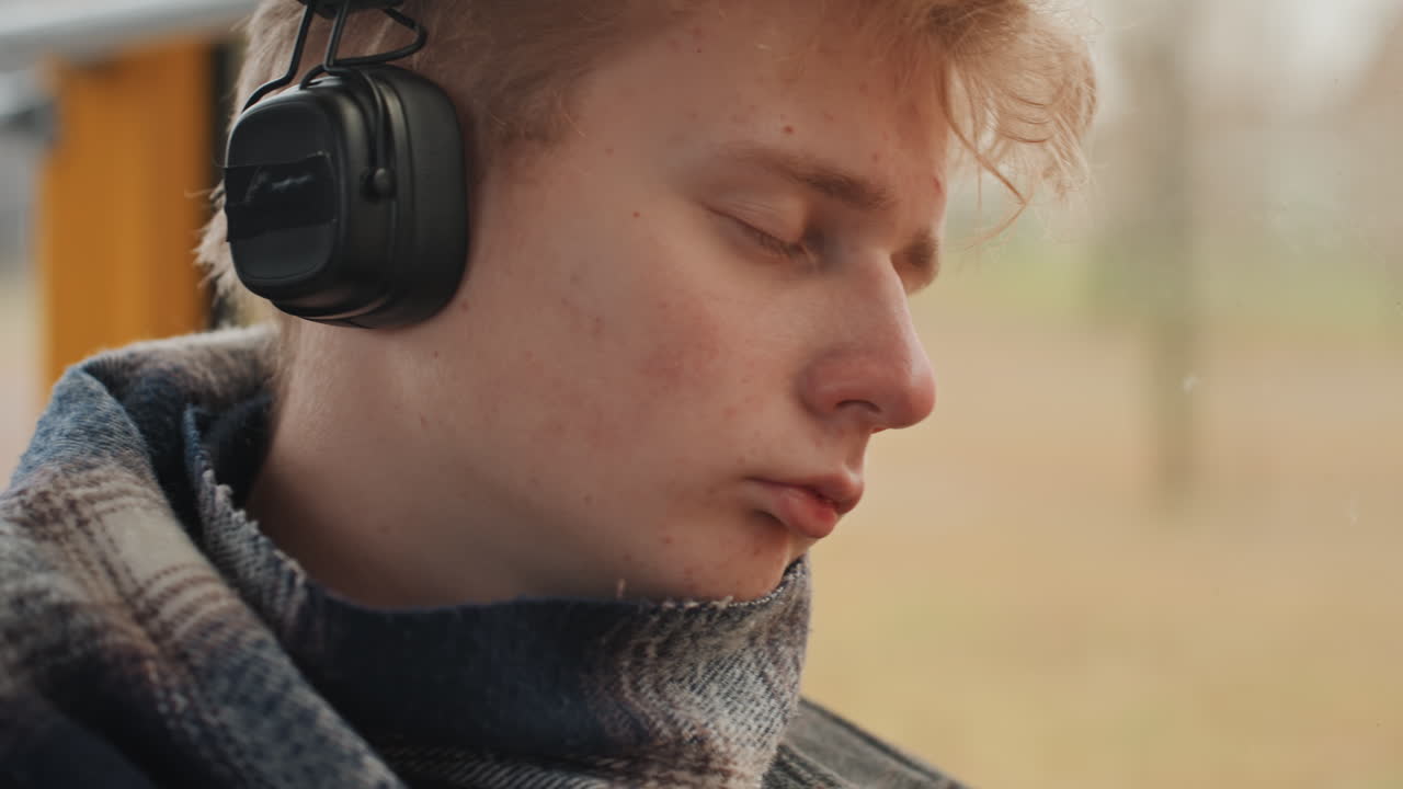 Individuo creativo immerso nella creazione musicale durante un viaggio. Giovane compositore perso nel suono mentre attraversa un parco. Artista appassionato che crea melodie sull'autobus con le cuffie e gli occhi chiusi.