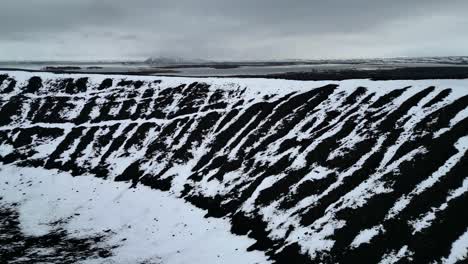cráter de volcán de piedra negra con manchas de nieve blanca en islandia desde el aire
