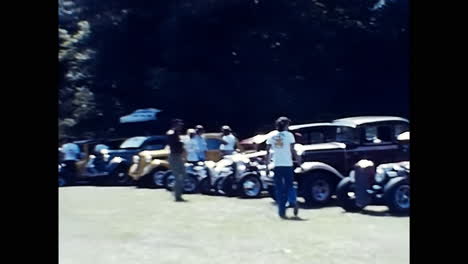 group of people observing a line of vintage cars at an old car show in the usa. circa usa - 1970s: a captivating photo capturing a group of individuals standing beside a row of parked classic cars from the 1970s at an old car show in the usa.