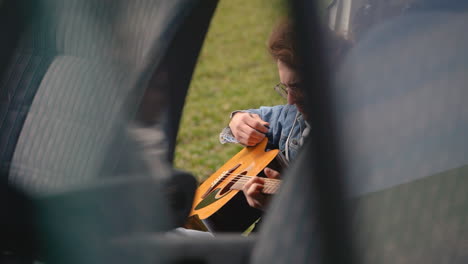 un joven con gafas toca la guitarra en la parte trasera de una caravana 2