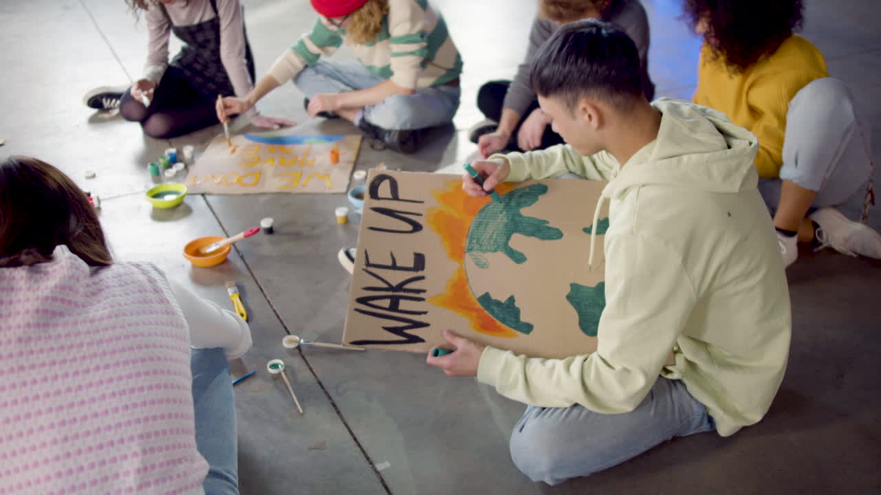 молодые экологические активисты рисуют плакаты, сидя на полу