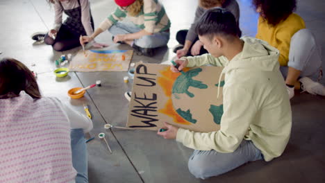 young environmental activists painting placards sitting on the floor